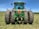 Farmer inspecting a green tractor in a lush agricultural field under clear skies.