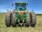 Farmer inspecting a green tractor in a lush agricultural field under clear skies.