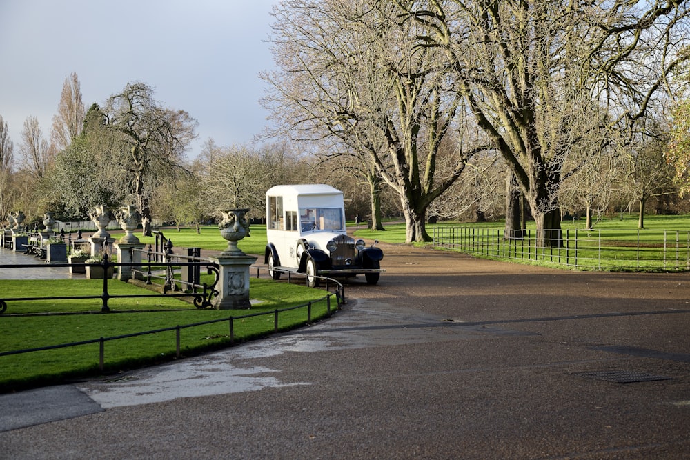 a white bus driving down a road next to a lush green park