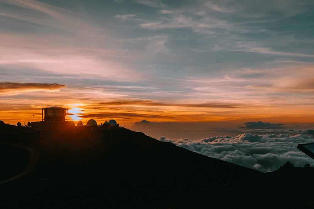 the sun is setting over the clouds above a mountain