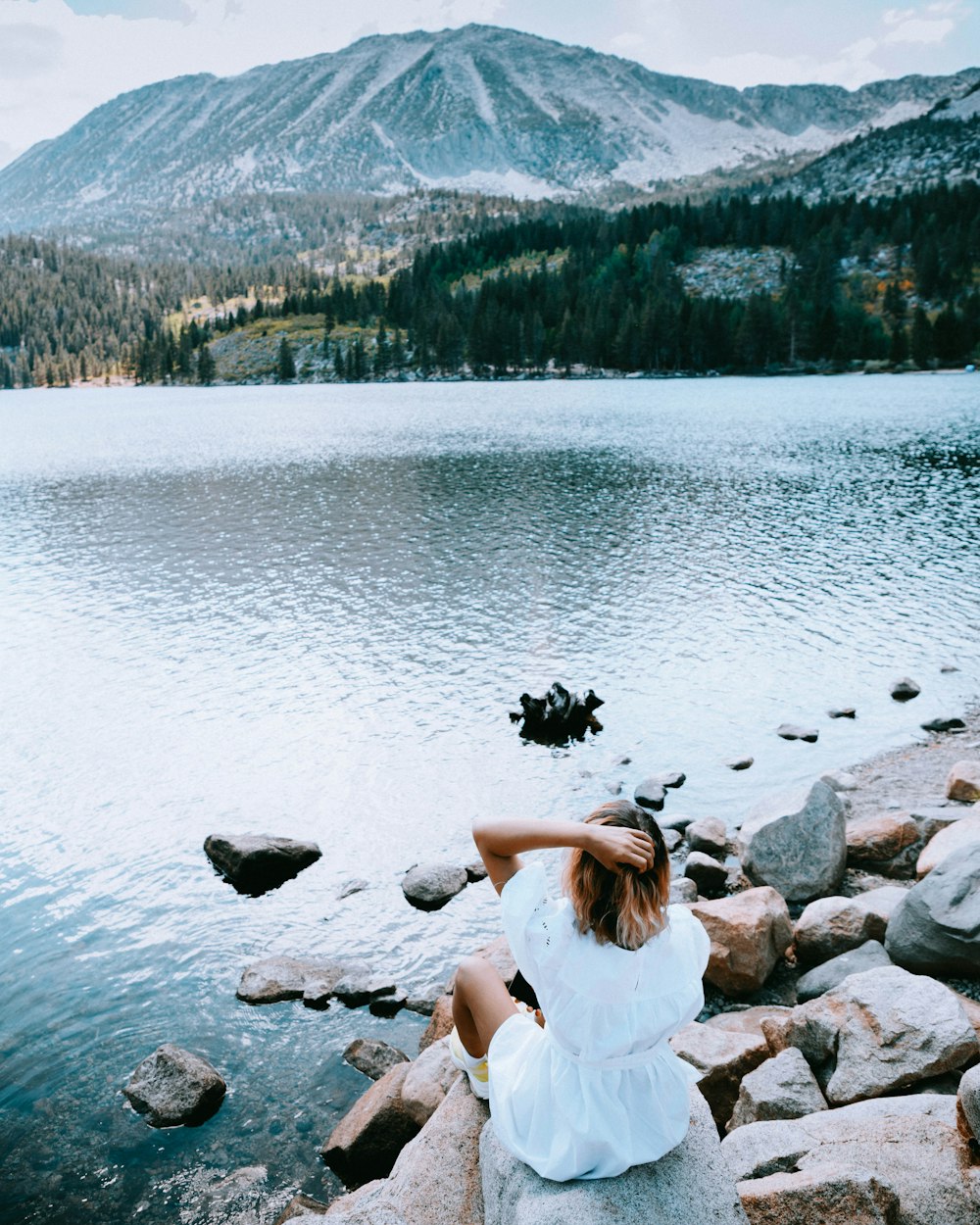 a woman sitting on a rock near a lake
