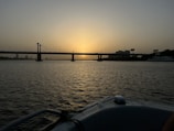 the sun is setting over a bridge over a body of water