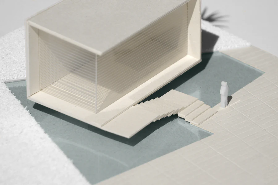 A white card model of a house with a pool and stepped terraces, on a teal base.