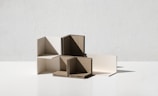 A minimalist composition featuring interlocking geometric shapes made from cardboard and white material, positioned on a flat surface with a plain background.