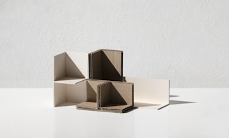 A minimalist composition featuring interlocking geometric shapes made from cardboard and white material, positioned on a flat surface with a plain background.