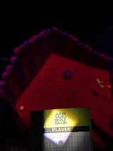 A dimly lit setting with a mini golf course featuring a red surface and a decorative enclosure around it. In the foreground, there is a scorecard with 'Junk Yard Golf Club' visible, and several names with scores written beside them. A small shadow partially obscures the card.