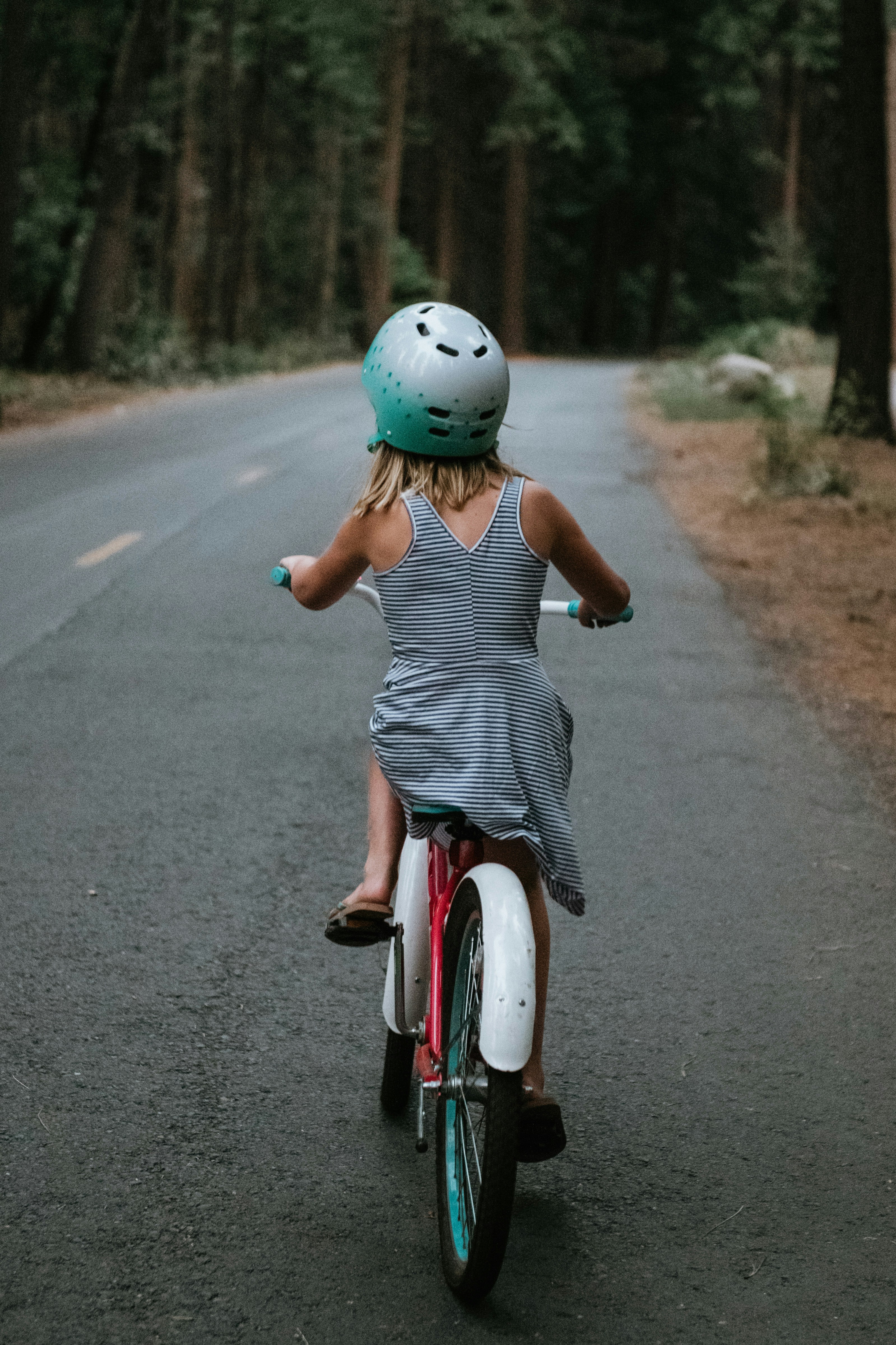 A young girl rides a bicycle down a forest road.