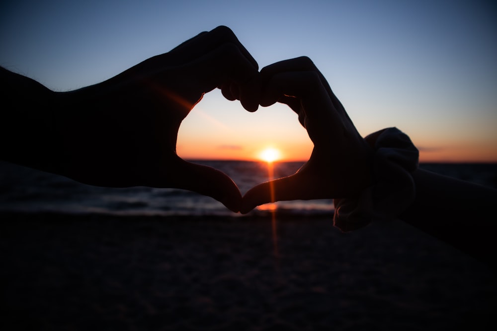 two hands making a heart shape with the sun setting in the background