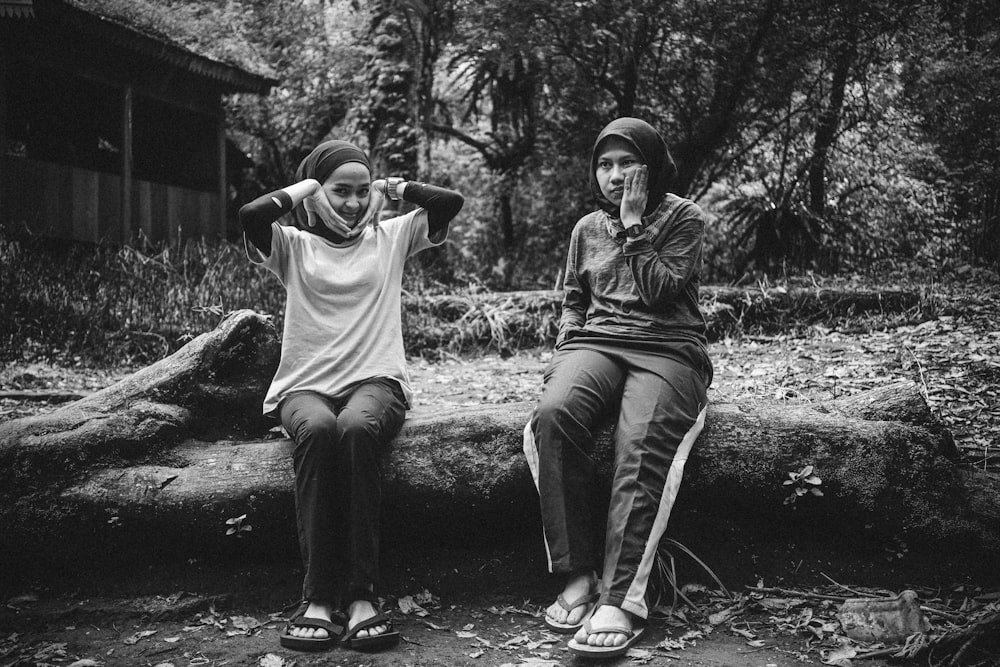 two women sitting on a log in the woods