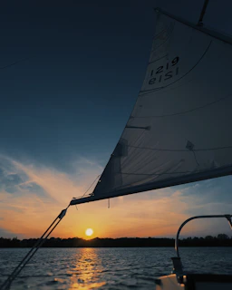 Sunset casting a warm glow over tranquil waters and distant sailboats.