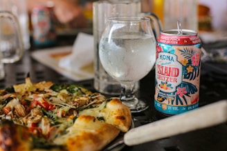 A chilled glass of soda with condensation droplets, next to a pizza slice.