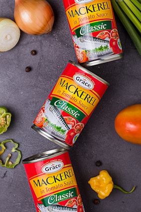 three cans of mackerel on a table next to some vegetables