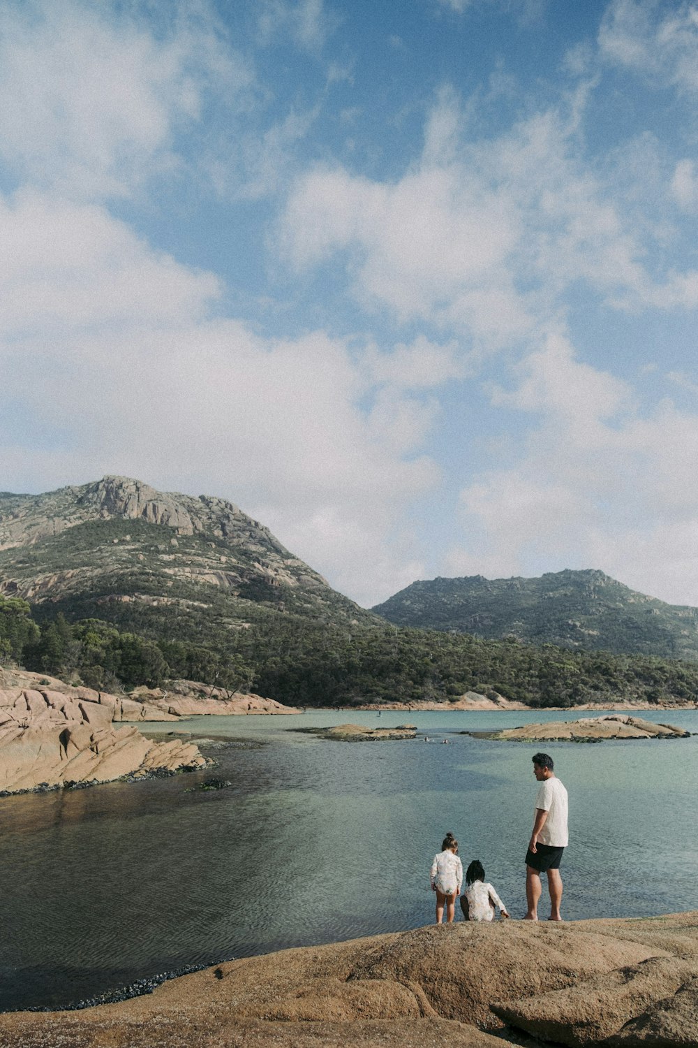 a group of people standing on top of a rock next to a body of water