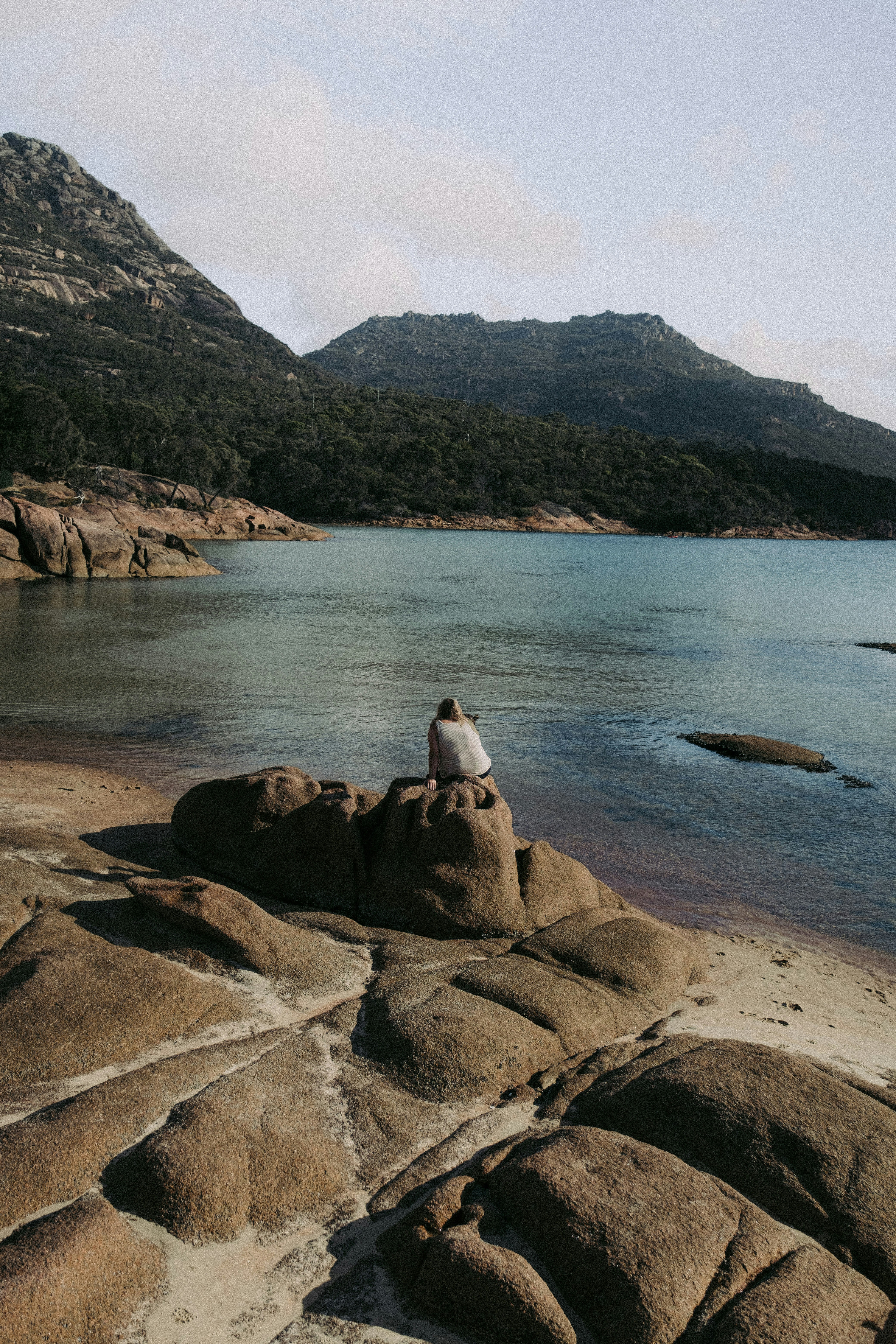 A person sitting on top of a rock near a body of water photo – Free ...