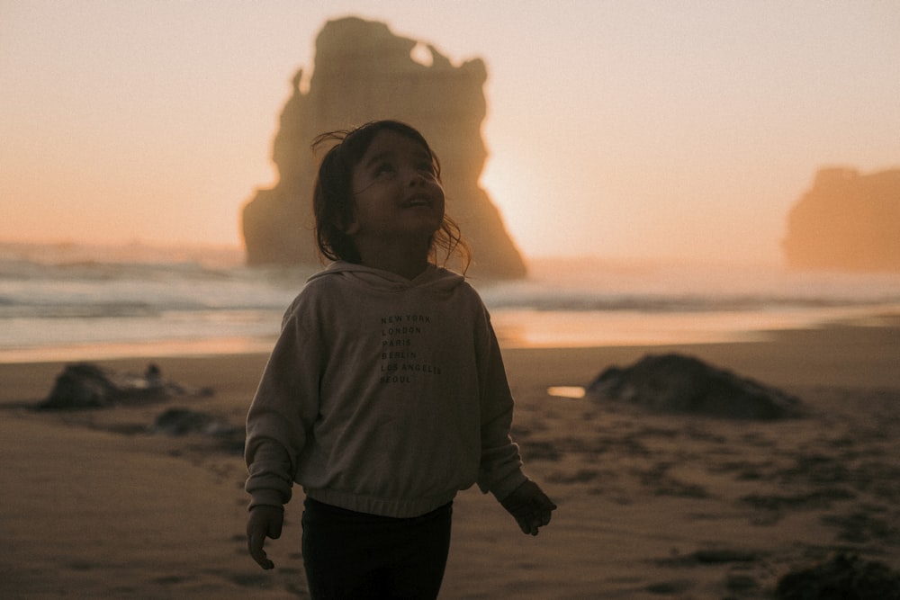 a little girl standing on top of a sandy beach