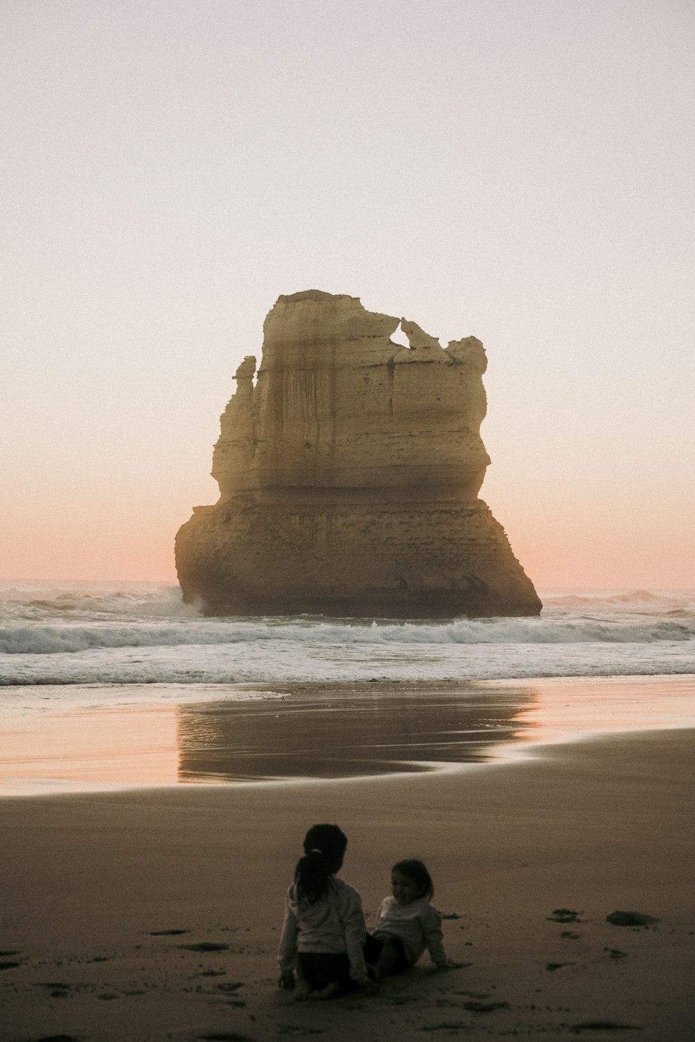 two children sitting on the beach watching the sun set