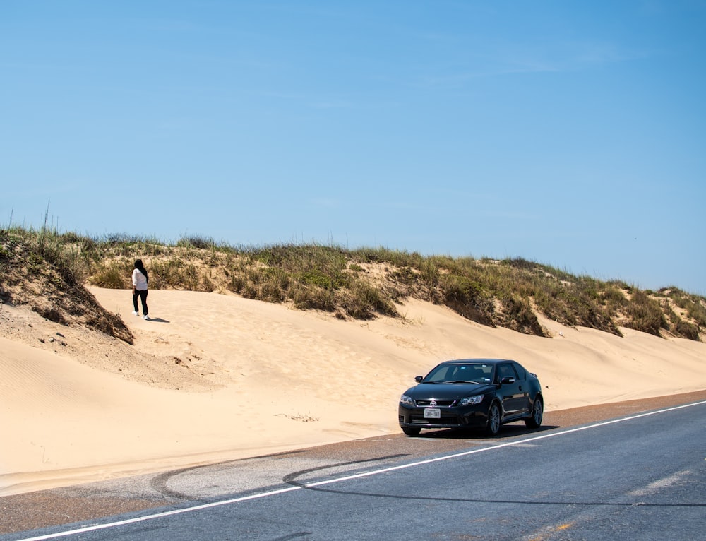 a car parked on the side of a road next to sand dunes