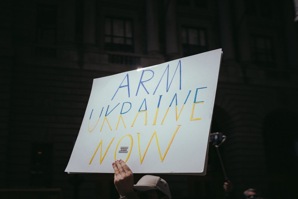 Eine Person, die ein Schild mit der Aufschrift "Arm Ukraine Now" hält