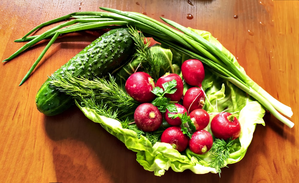 a wooden table topped with lettuce, radishes and cucumbers