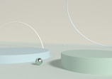 An abstract composition featuring two circular platforms of different sizes placed on a flat surface, accompanied by a pearl-like sphere. Large, thin arcs create a minimalist geometric design against a subtle, single-tone backdrop.