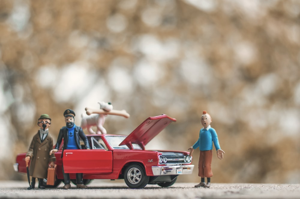 a group of toy people standing next to a red truck