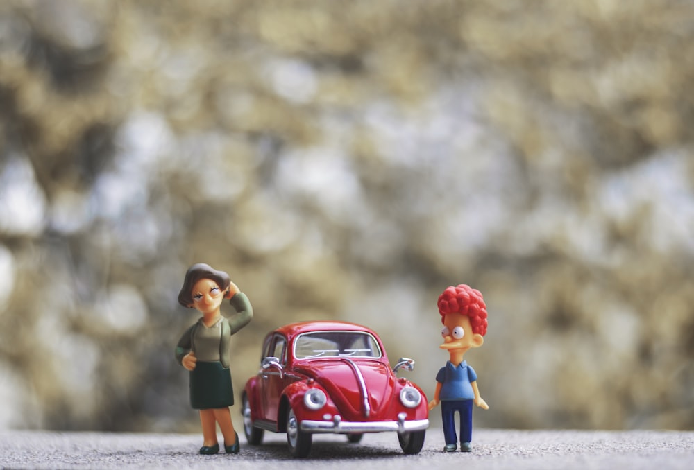 a couple of figurines standing next to a red car