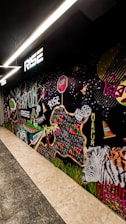 A vibrant mural featuring various elements such as a zebra, traffic cones, dice, a stop sign, and colorful text reading 'Rise,' 'Mirpur,' and 'Dhaka.' The artwork incorporates dynamic shapes, patterns, and graffiti-style lettering, creating an urban and energetic scene.