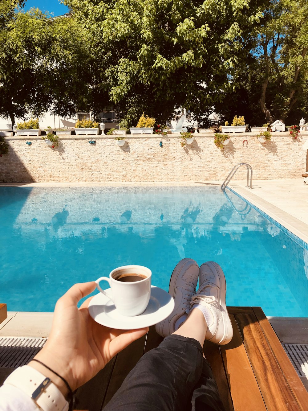 a person holding a cup of coffee next to a swimming pool