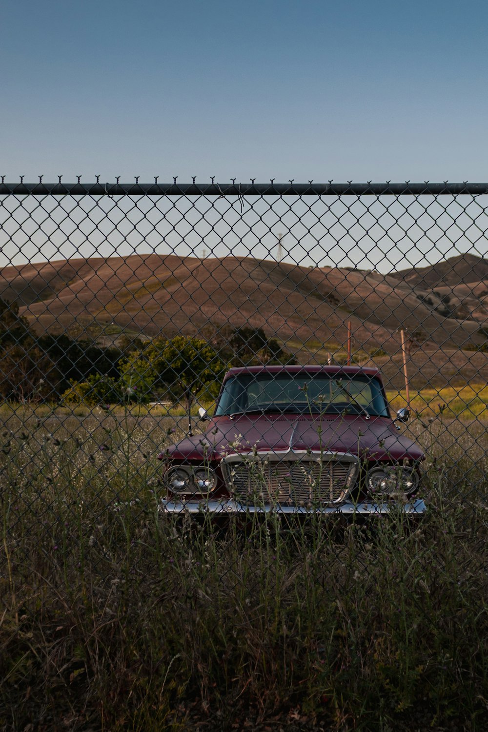 an old car parked in a field behind a chain link fence