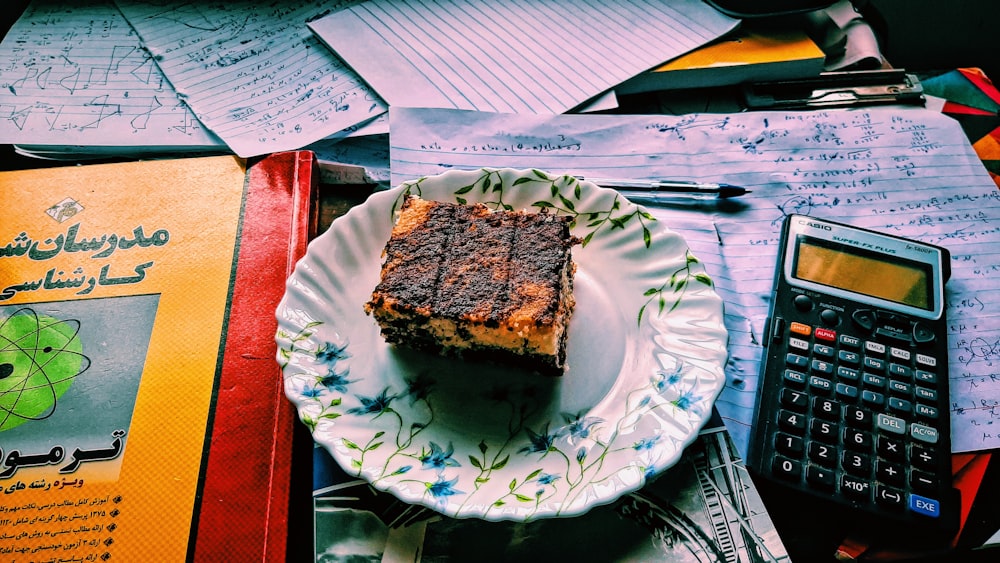 a piece of cake on a plate next to a calculator