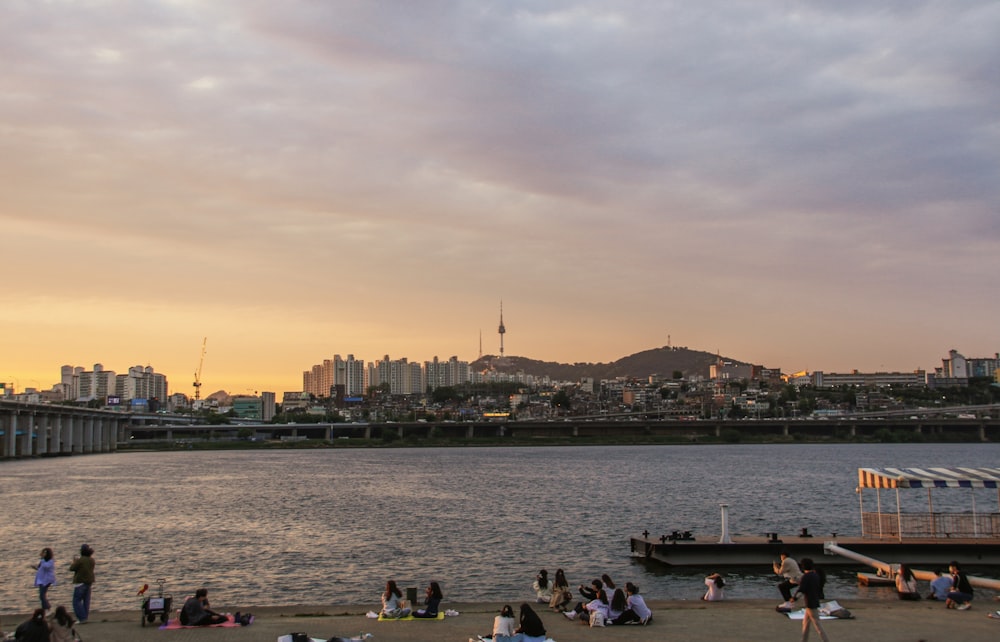 a group of people sitting on a beach next to a body of water