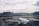 An airplane from Turkish Airlines is parked at an airport gate, surrounded by various ground service vehicles. The terminal building stretches across the background under a partly cloudy sky.