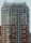 A high-rise building with a modern architectural design featuring a grid of windows and a mix of beige and brown tones. The structure has a distinctive top with vertical protrusions and a rooftop area that may include utility equipment.
