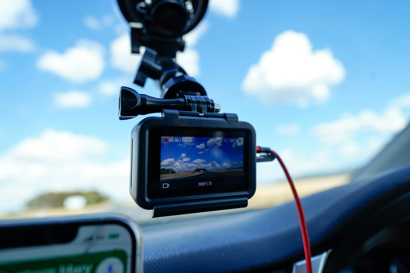 A small dash camera mounted to a car windshield behind the rearview mirror