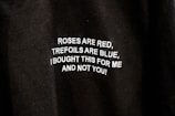 A close-up of a black fabric with white text embroidered on it. The text reads: 'ROSES ARE RED, TREFOILS ARE BLUE, I BOUGHT THIS FOR ME AND NOT YOU!'