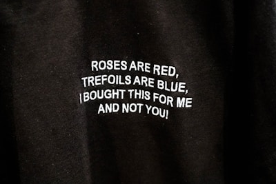 A close-up of a black fabric with white text embroidered on it. The text reads: 'ROSES ARE RED, TREFOILS ARE BLUE, I BOUGHT THIS FOR ME AND NOT YOU!'