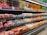 A supermarket produce section displays a neatly organized assortment of fruits. The shelves are filled with apples, grapes, pears, oranges, and other fruits, each packed in individual wrapping or foam nets. Pricing labels are visible above the fruits, indicating price per kilogram.
