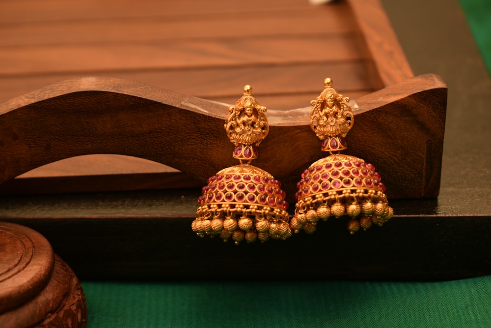 a pair of red and gold earrings sitting on top of a wooden stand