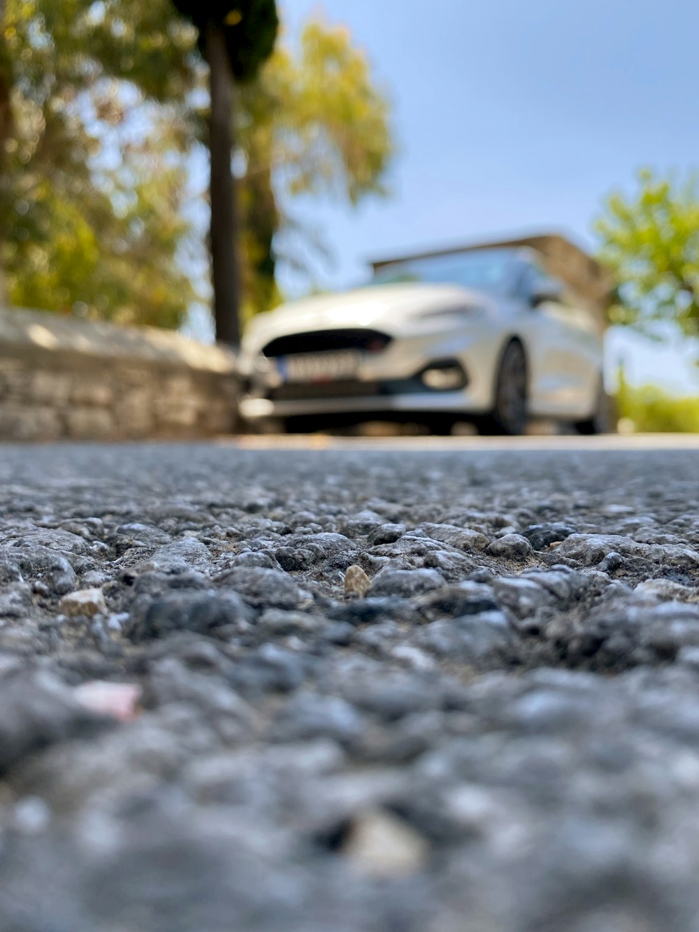 a white car driving down a street next to a stone wall