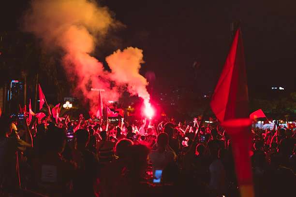 A vibrant crowd at a Kerala political rally waving flags under dramatic red and gold lighting.