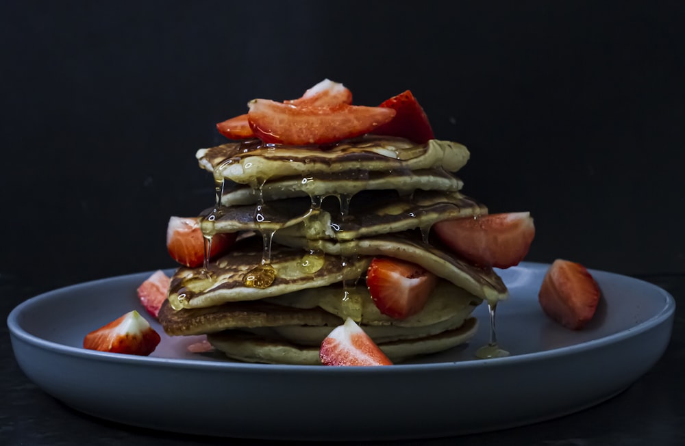a stack of pancakes covered in syrup and sliced strawberries