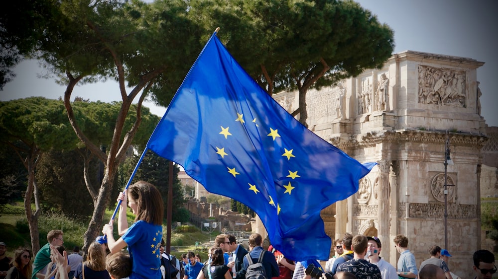 a young girl holding a european flag in front of a crowd of people