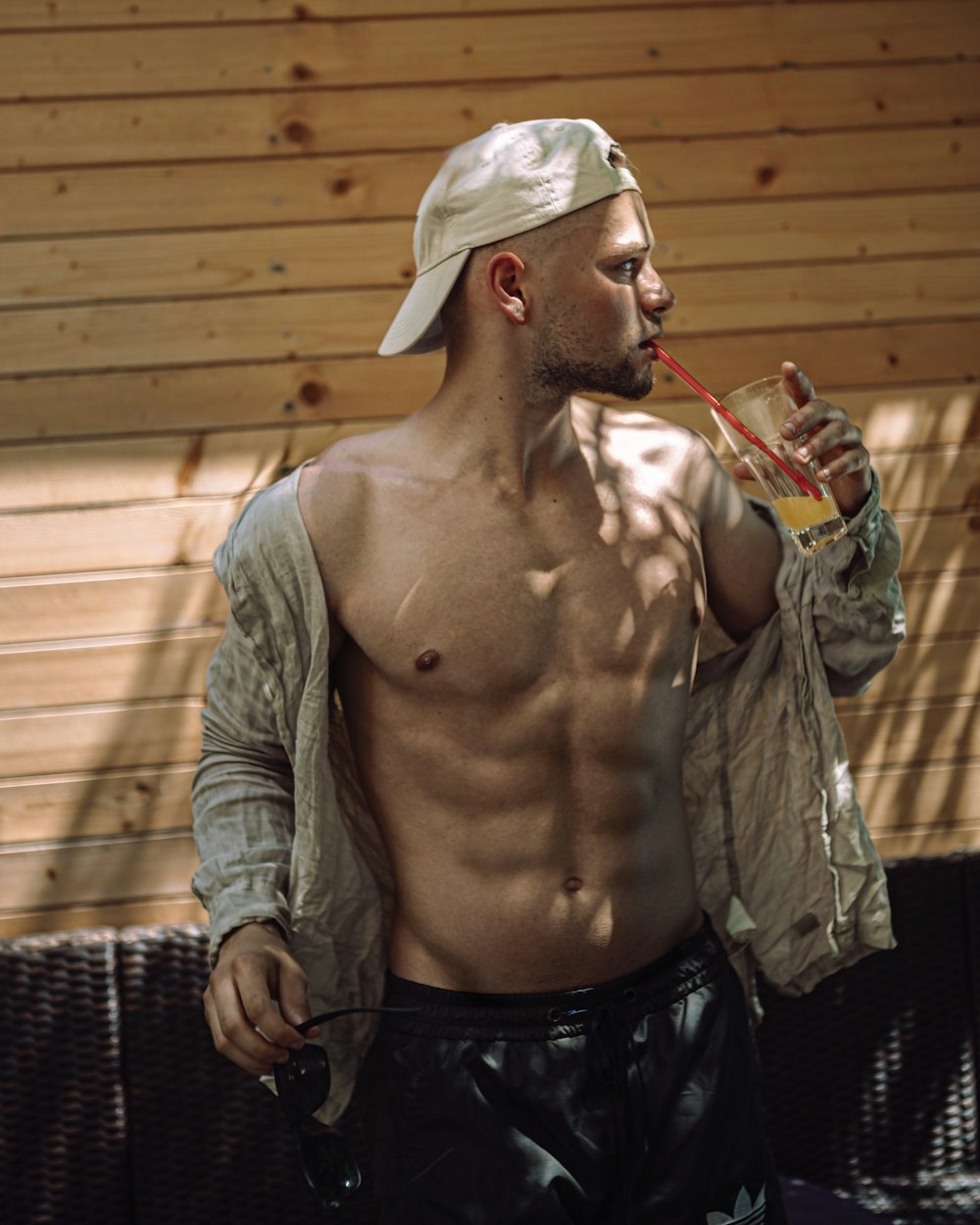 a shirtless man drinking a drink from a straw