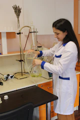 a woman in a lab coat pouring liquid into a beakle