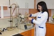 a woman in a lab coat pouring liquid into a beakle
