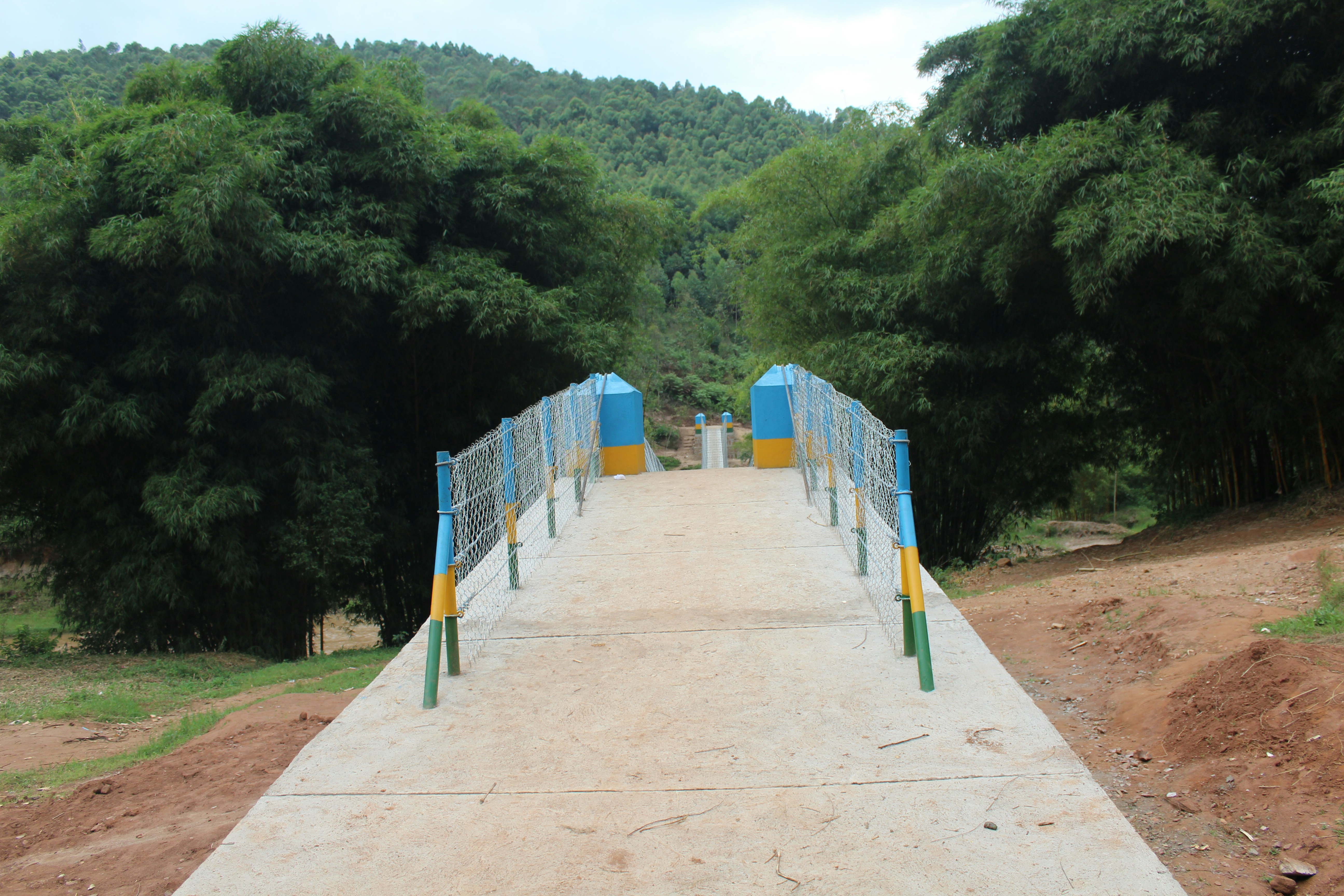 a blue and yellow bridge over a dirt road