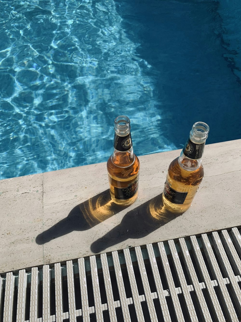 two bottles of beer sitting next to a swimming pool