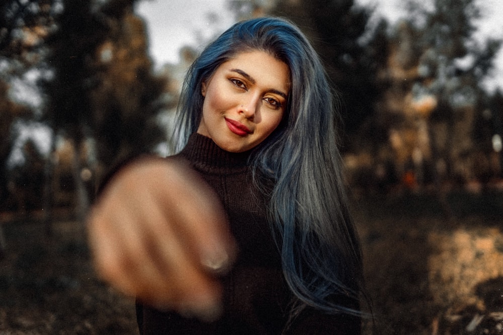 a woman with blue hair pointing at the camera