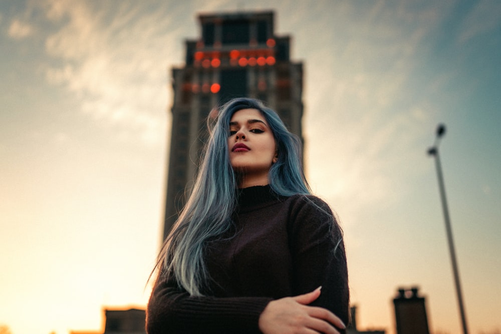 a woman with blue hair standing in front of a tall building