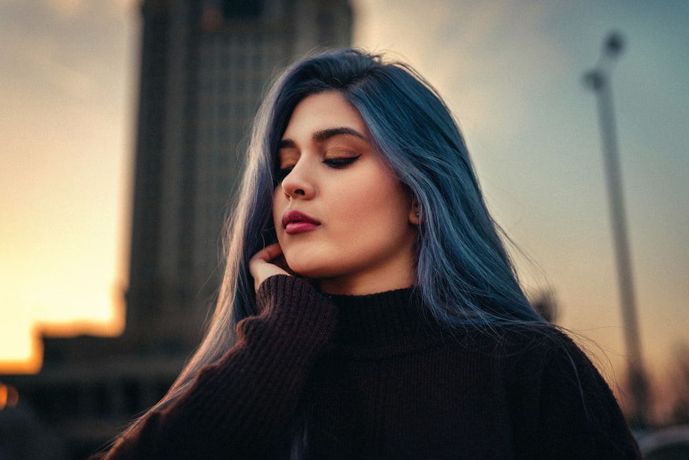 Eine Frau mit langen blauen Haaren steht vor einem hohen Gebäude